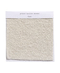 A square Fabric Swatch Oyster Mini Boucle, showcasing textured off-white boucle fabric used on pieces like the Upholstered Cove Bed, is displayed against a white background.