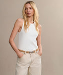 A woman with long blonde hair, wearing a white sleeveless top and light beige pants, stands against a neutral background. She accessorizes with the Mini Jules Belt, known for its chic rope-twist belt buckle.