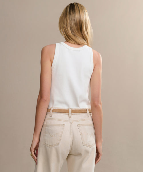 A person with long blonde hair is seen from behind, wearing a white sleeveless top and high-waisted light beige jeans, styled with the Mini Jules Belt, against a plain beige background.
