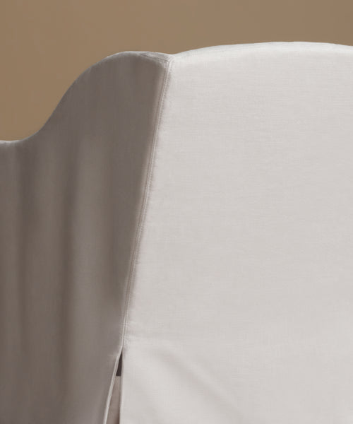 A white upholstered armchair with a matching back cushion, shown against a solid warm taupe background.