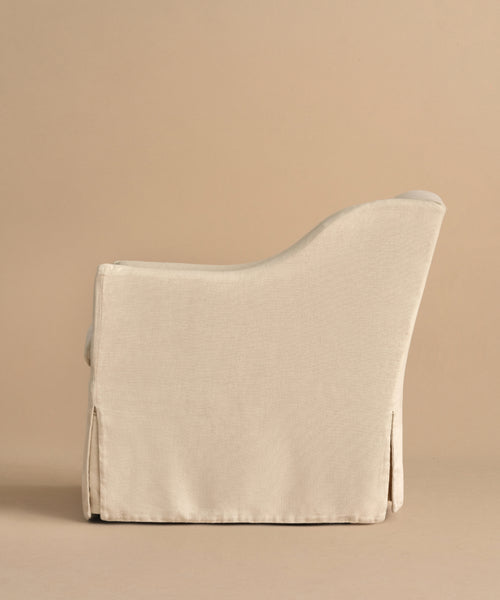 A side view of the Miramar Chair, upholstered in beige Belgian linen with a tailored slipcover, featuring a smooth, rounded back and armrest in a minimalist modern design, set against a matching beige background.