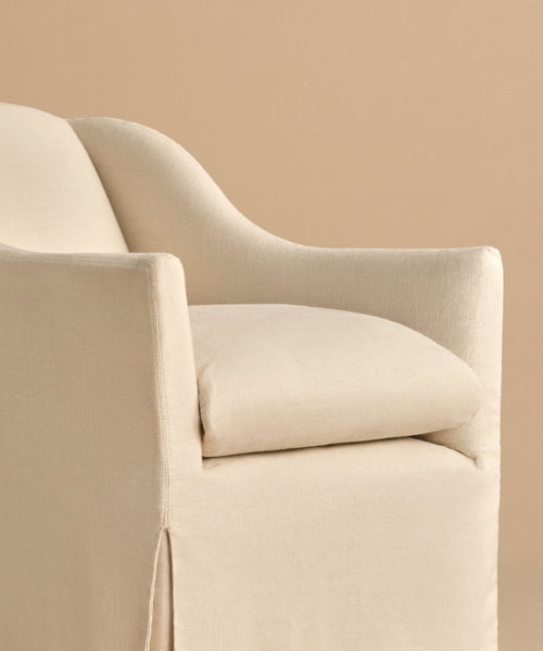 A close-up of the Miramar Chair showcases its modern, cream linen slipcover, curved back, and cushioned seat, set against a beige background.