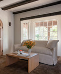 A living room setting with a light natural upholstered sofa, oak wood coffee table and a dark rug. 