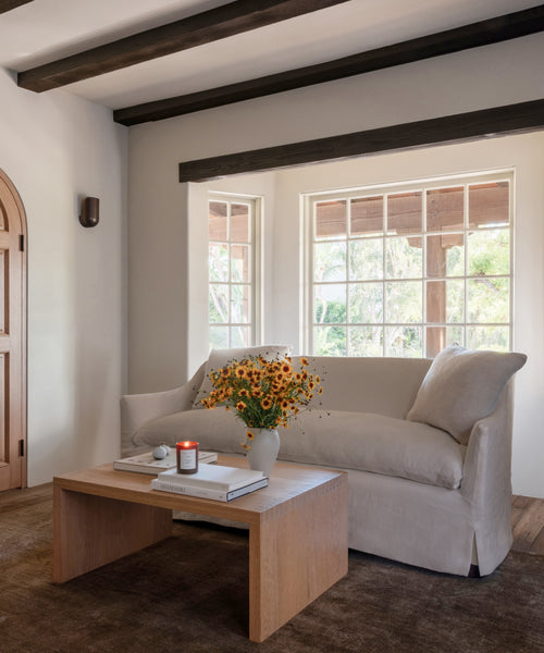 A living room setting with a light natural upholstered sofa, oak wood coffee table and a dark rug. 