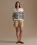Woman wearing a striped cardigan and beige shorts against a plain background