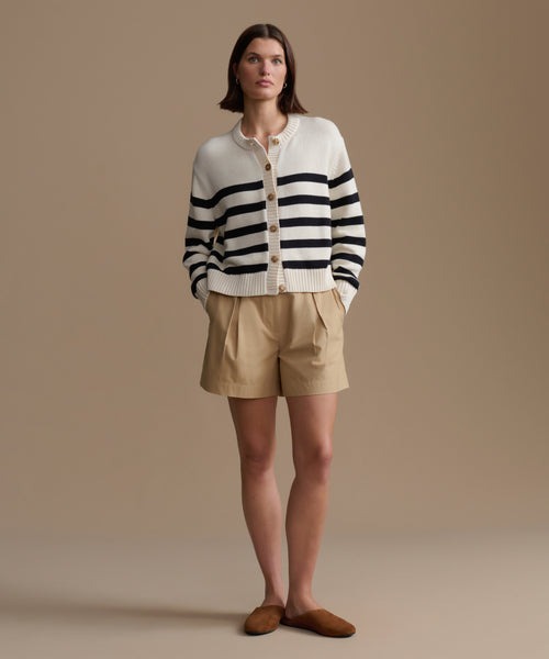 Woman wearing a striped cardigan and beige shorts against a plain background