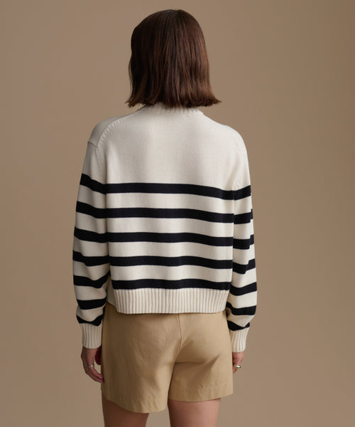 Woman wearing a black and white striped sweater with beige shorts on a brown background