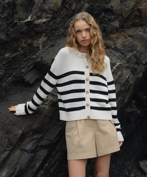 Woman wearing a black and white striped sweater and beige shorts standing against a rocky background