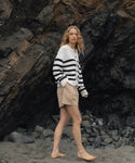 Woman in a striped sweater and shorts standing on a rocky beach.