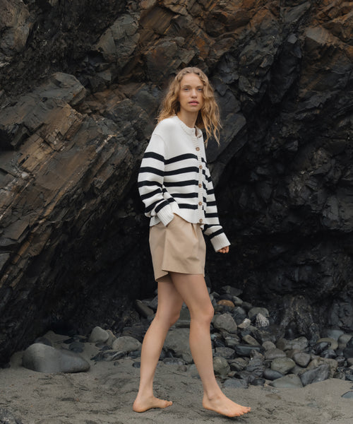 Woman in a striped sweater and shorts standing on a rocky beach.