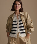 Woman wearing a beige trench coat over a striped cardigan on a beige background