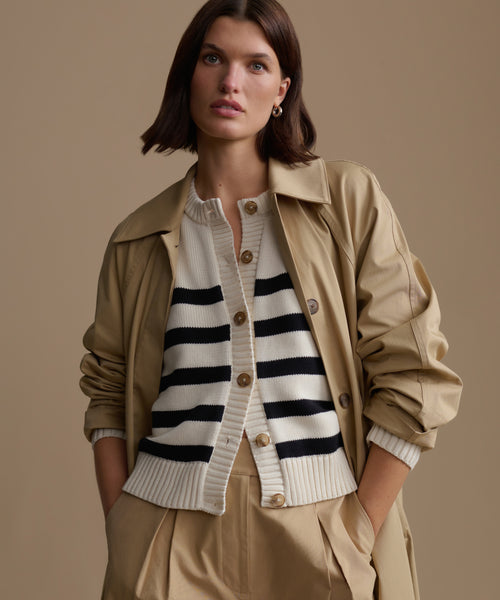 Woman wearing a beige trench coat over a striped cardigan on a beige background
