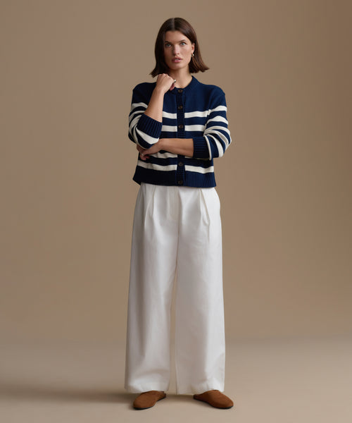 Woman wearing a striped sweater and white pants against a beige background