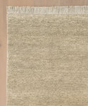 A close-up of the Mojave Jute Rug, featuring beige tones, horizontal lines, and fringed edges on a light wooden floor. Only part of the rug is visible, highlighting its handcrafted weave and detailed fringe.