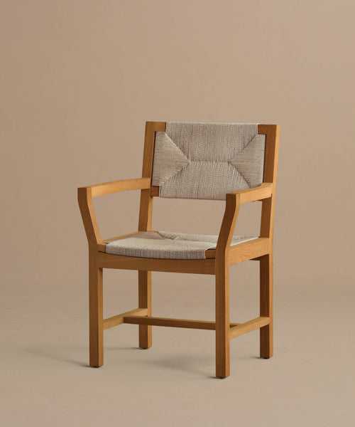 The Outdoor Montecito Dining Arm Chair Frame, crafted from teak with a natural finish and beige woven fabric padding, sits against a plain beige background. Made with ECOLENE materials for durability and corrosion resistance outdoors.