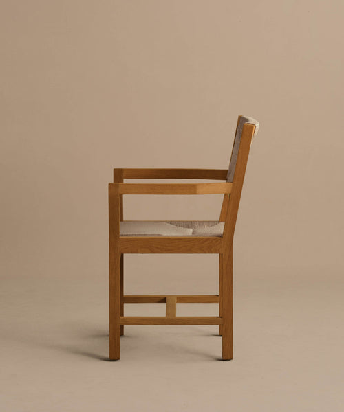 The Outdoor Montecito Dining Arm Chair Frame is shown in profile against a beige background, featuring clean lines, a modern design, and corrosion-resistant materials for lasting durability. Beige cushioned seat and backrest included.