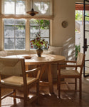 Dining chairs set with a round oak dining table with flowers in a dining room setting.