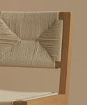 A close up image of a warm oak dining chair against a beige background.