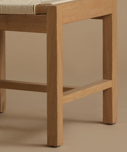 A close up image of a warm oak dining chair against a beige background.