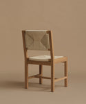 The back of a warm oak dining chair against a beige background.
