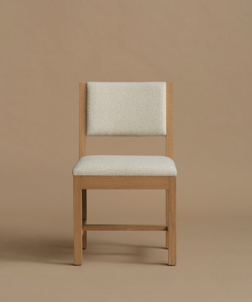 An ivory upholstered dining chair with oak wood set against a beige background.