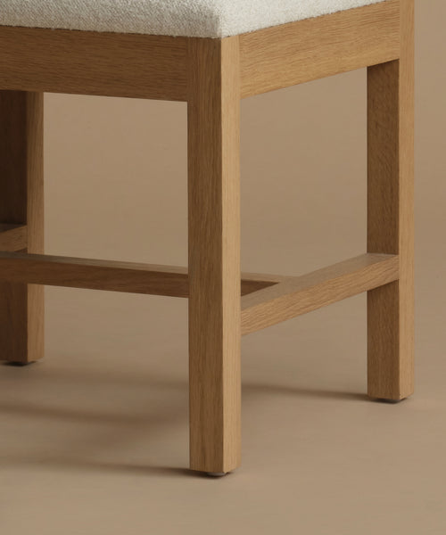 A close up of an ivory upholstered dining chair with oak wood set against a beige background.