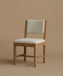 An ivory upholstered dining chair with oak wood set against a beige background.