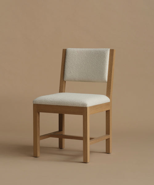 An ivory upholstered dining chair with oak wood set against a beige background.