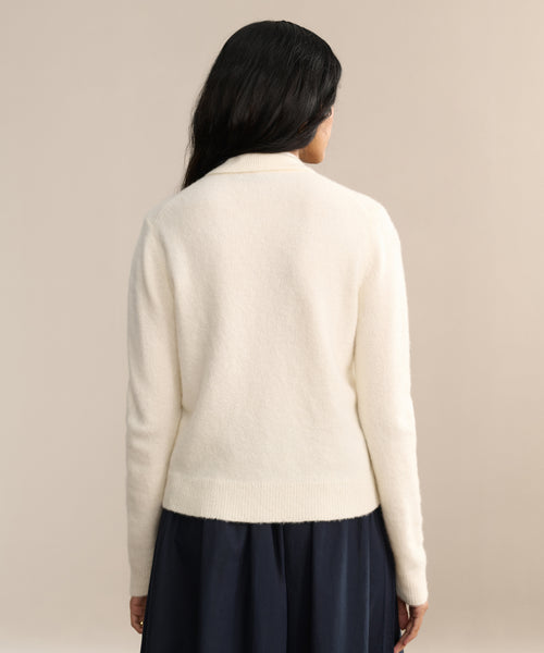 A person with long dark hair is standing with their back to the camera against a neutral background, wearing the Murphy Cardigan in ivory and a dark skirt.