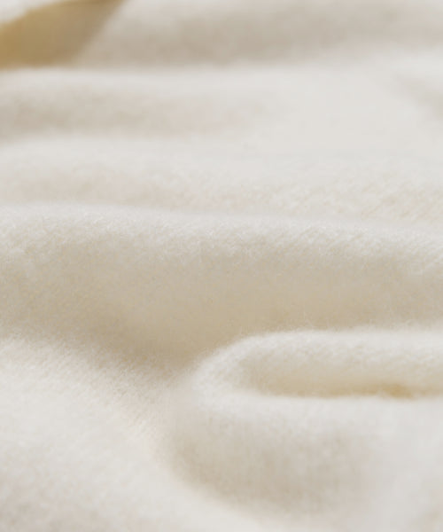 A close-up of the Murphy Cardigan’s soft, creamy white fabric with gentle folds and a slightly fuzzy texture evokes the warmth and comfort of an ivory sweater.