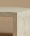 A close up of an ivory parchment coffee table with natural detailing against a beige background.