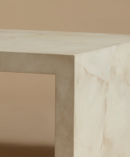 A close up of an ivory parchment coffee table with natural detailing against a beige background.
