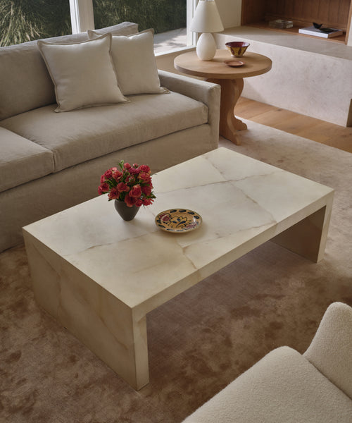 An ivory parchment coffee table in a living room setting with a natural upholstered sofa. 