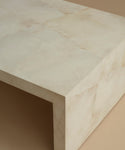 A close up of an ivory parchment coffee table with natural detailing against a beige background.