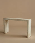 A minimalist console table made of light beige parchment with subtle white veining, set against a solid warm beige background.