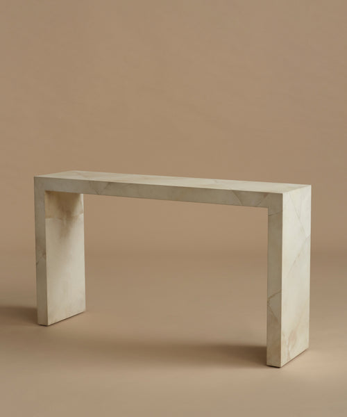 A minimalist console table made of light beige parchment with subtle white veining, set against a solid warm beige background.