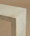 A a close up of a minimalist console table made of light beige parchment with subtle white veining, set against a solid warm beige background.