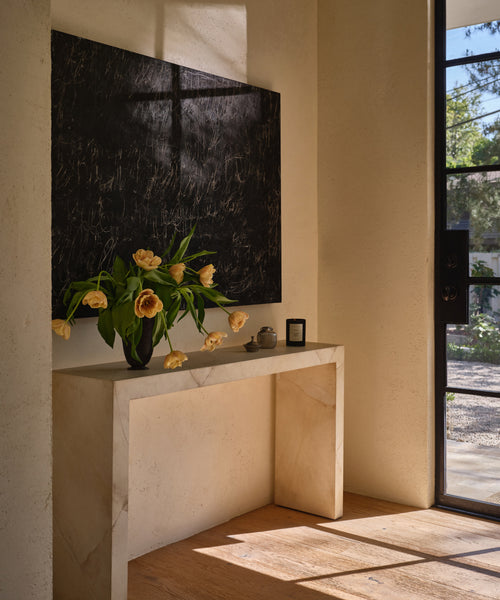 An entryway including a parchment console table with a vase and flowers.