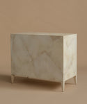 A dresser with a cream-colored bone inlay pattern on a rectangular cabinet, supported by four tapered legs, set against a solid beige background.