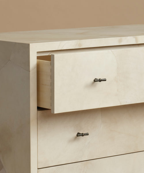 Close-up of a cream-colored marble dresser with two drawers pulled out, featuring dark metal knobs against a neutral beige background.
