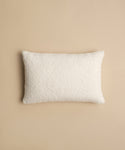 The Nell Boucle Lumbar Pillow, a rectangular ivory pillow with a textured finish, is centered on a plain beige background.