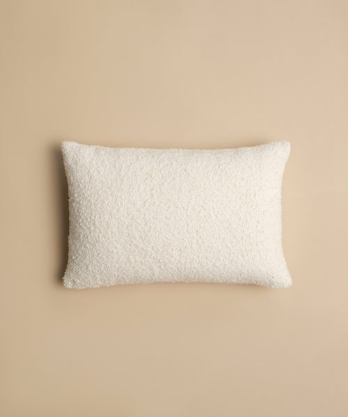 The Nell Boucle Lumbar Pillow, a rectangular ivory pillow with a textured finish, is centered on a plain beige background.