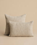 Two rectangular beige Nell Boucle Lumbar Pillows are set against a matching background, with one slightly overlapping the other to showcase their natural boucle texture.