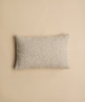 A Nell Boucle Lumbar Pillow with a rectangular, textured beige design is centered on a matching beige background.