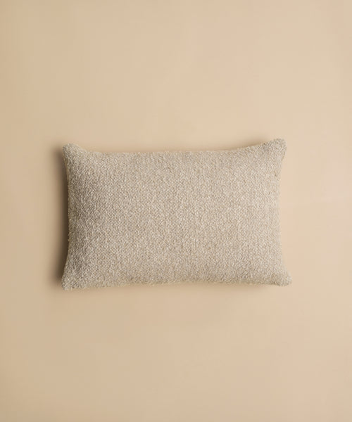 A Nell Boucle Lumbar Pillow with a rectangular, textured beige design is centered on a matching beige background.