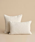 Two Nell Boucle pillows in ivory are arranged on a beige surface with a matching background, one slightly in front of and overlapping the other.