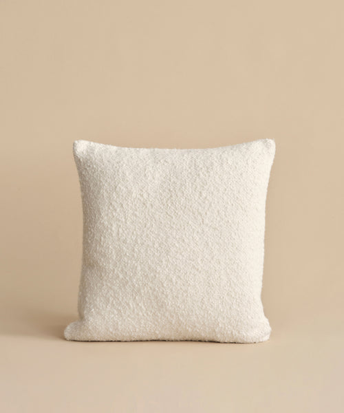 The Nell Boucle Pillow—a square, textured ivory accent—is centered against a plain beige background.