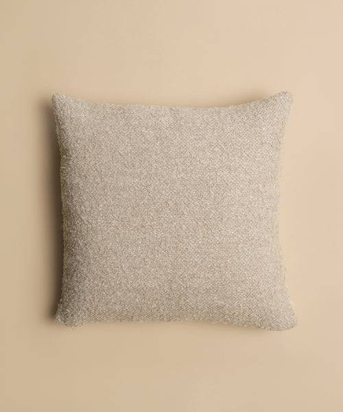 The Nell Boucle Pillow, a square textural cushion in beige, is shown from above on a solid light tan background.