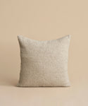 The Nell Boucle Pillow, a beige square pillow with a textured finish, is displayed against a matching background. Its minimalist design is natural and simple, with no visible patterns or embellishments.