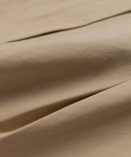 A close-up of light brown Italian cotton poplin shows smooth, matte texture and soft folds. The fabric is gently creased, with shadows and highlights—ideal for summer wear like the Newport Short.